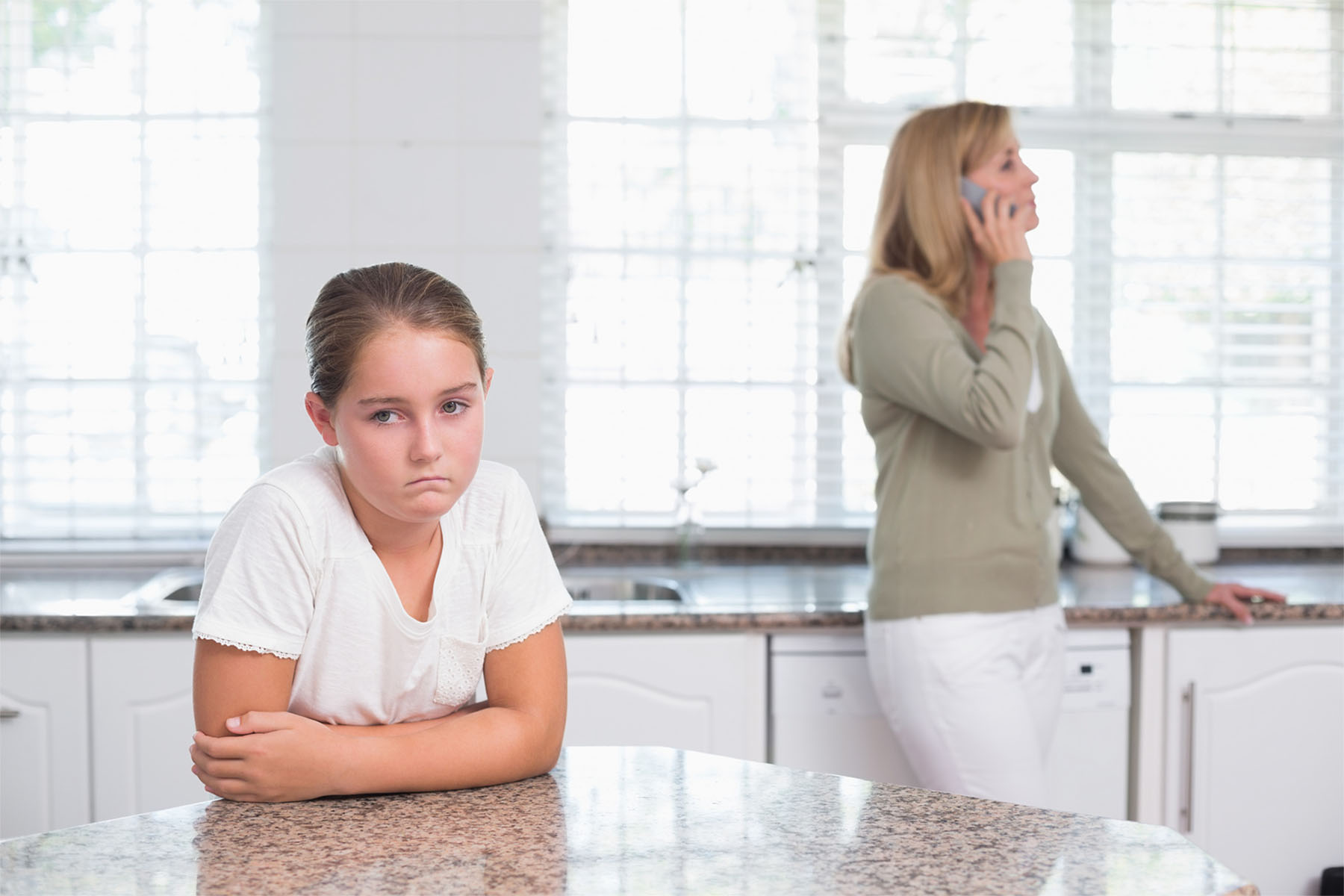 Mother on the phone while daughter sulking at home in the kitchen